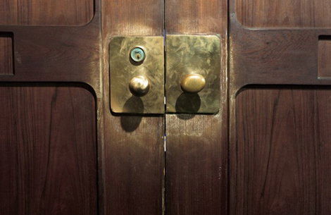 Two brass door knobs are set into square plates on a pair of dark wood doors. A small keyhole is visible above the left knob.