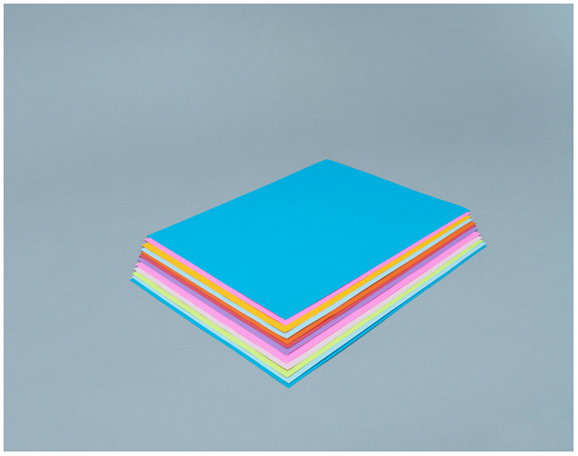 A stack of brightly coloured square sheets of paper on a plain grey background. The top sheet is blue, followed by layers of orange, pink, yellow and light blue.