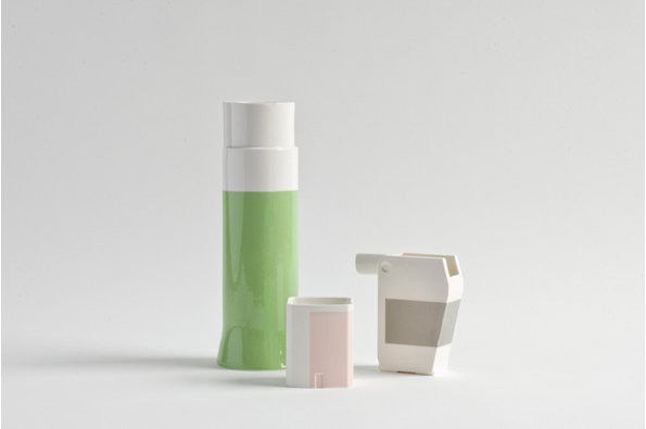 Three ceramic vessels of varying heights and shapes stand against a plain white background. The tallest is a slender green cylinder with a white top, flanked by two smaller white pieces with pink and grey accents.