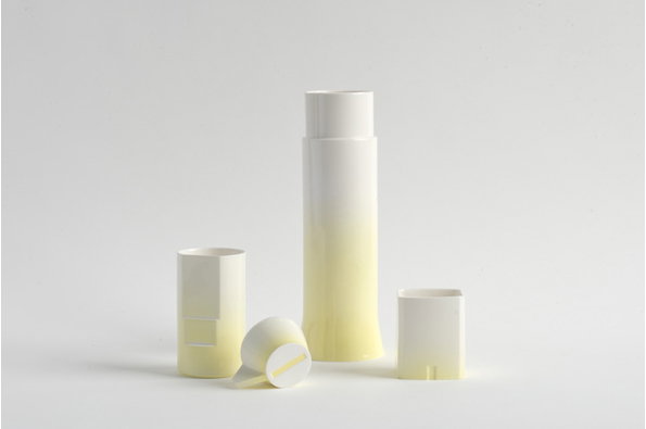 Four white ceramic vessels of varying heights and shapes stand against a plain light grey backdrop. The tallest cylinder features a soft yellow gradient fading upwards into white.