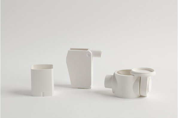 Three white ceramic vessels with geometric, architectural shapes are arranged against a plain white background. The pieces feature clean lines and hollowed-out sections, resembling minimalist sculptures.