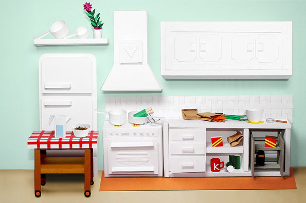 A 3D render of a kitchen scene constructed entirely from white paper. A red and white checked tablecloth covers a small wooden table, while paper cut-outs form the fridge, oven and cupboards.