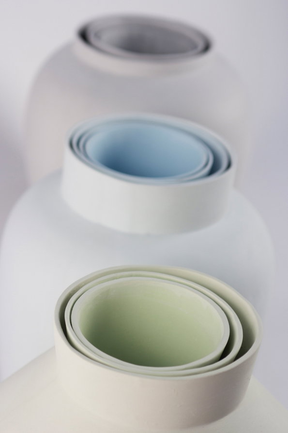 Three ceramic vases are arranged in a row against a plain white background. Each vase has a wide, spiralling rim in a different pale shade of grey, blue and green.