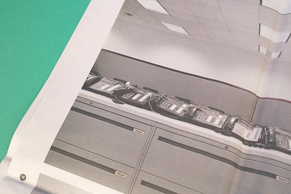 A row of vintage office telephones sits on a grey desk in a sterile, white office. The image is a photograph of a page in a book, set against a green background.