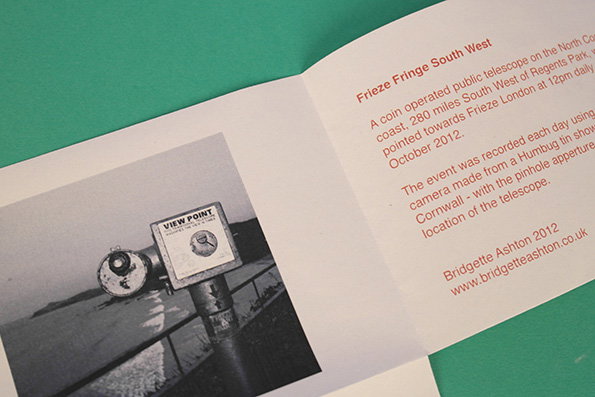 A folded white brochure rests on a green surface. It features a black and white photograph of a public telescope at a “View Point” and text titled “Frieze Fringe South West”.