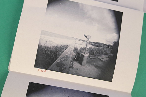A black and white photograph in a printed booklet shows a scenic overlook with a coin-operated telescope. Below the image, small red text reads “Day 4”.