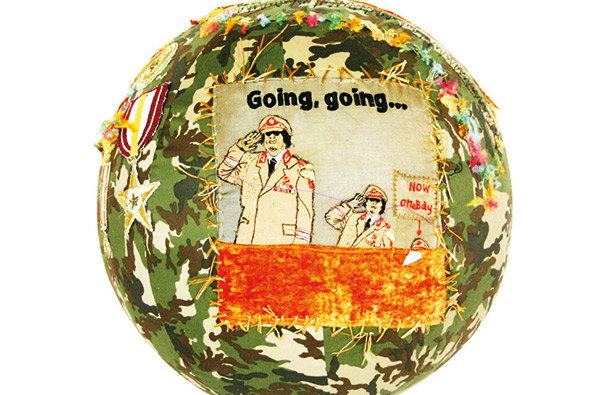 A camouflage fabric circle features a stitched-on illustration of two figures in military uniforms saluting. Above them, the text reads “Going, going...”, while a small speech bubble says “Now on bay”.