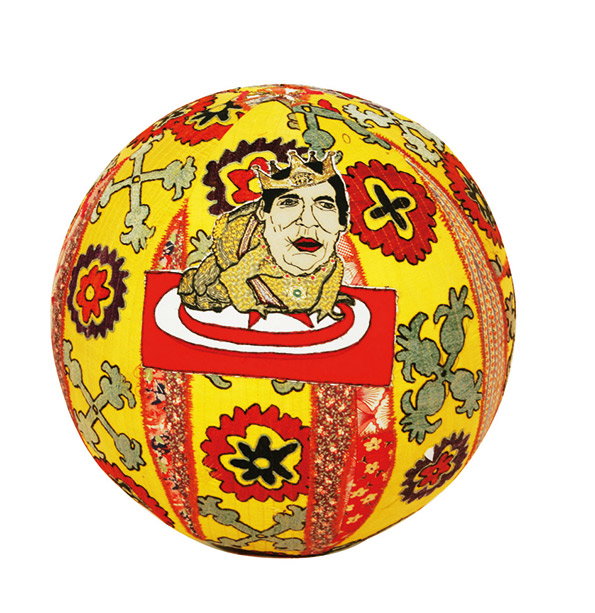 A spherical sculpture covered in yellow and red patterned fabric. A central image shows a figure wearing a crown, resting on a red rectangular base.