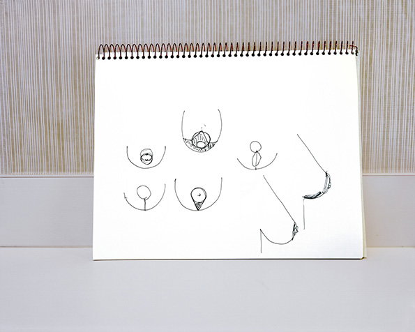 A sketchbook open to a page of simple line drawings. The sketches show various perspectives and shapes of breasts and nipples.