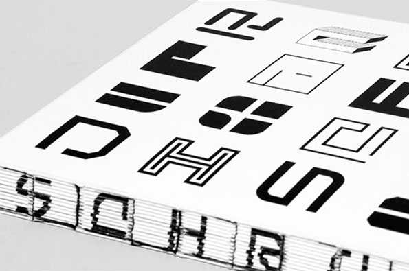 A close-up of a book cover featuring a grid of bold, black abstract glyphs on a white background. The side of the book shows the word “SCHRIFT” printed across the edges of the pages.