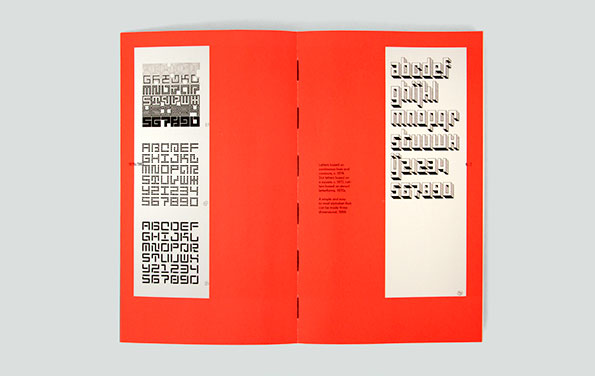 An open book with bright red pages displays various typeface specimens. The left page shows three different blocky, geometric alphabets, while the right page features a rounded, 3D-style font.