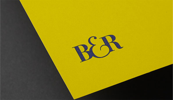 A yellow card features a dark blue logo reading “B&R”. The card is angled across a dark grey background.