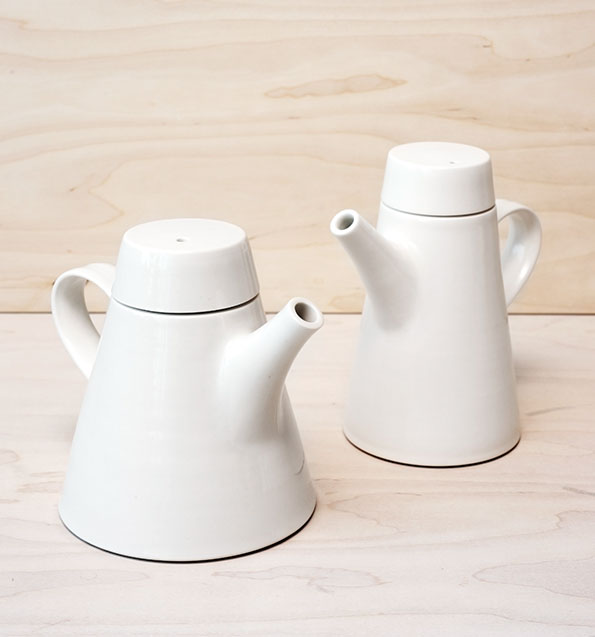 Two white ceramic teapots with tapered bodies and matching lids. They sit on a light wood surface against a matching wooden backdrop.