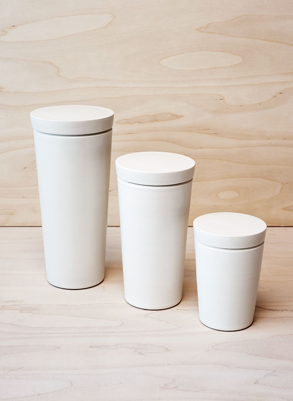 Three white cylindrical canisters of varying heights stand in a row. They are set against a light-coloured plywood background.