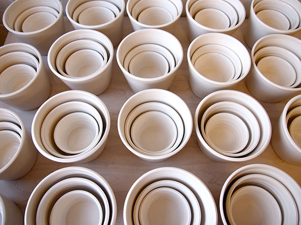 Rows of off-white ceramic bowls are nested inside one another. The bowls are arranged in a neat grid across a plain surface.