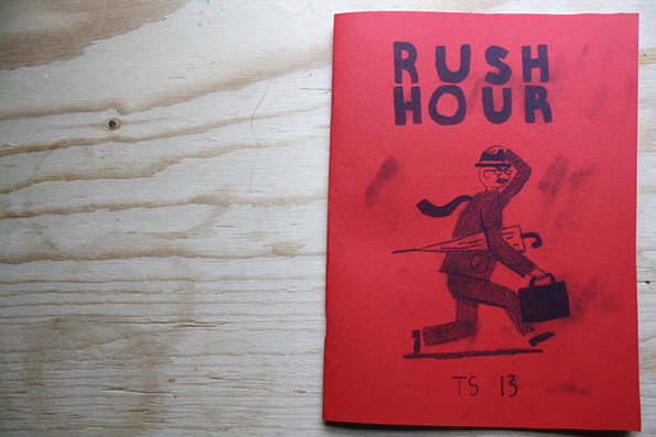 A red booklet lies on a light wood surface. The cover features a bold illustration of a person in a suit and hat carrying a briefcase and umbrella, with the words “RUSH HOUR” printed above.