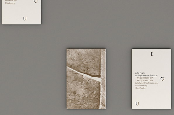 Three business cards are arranged on a grey surface. One card shows a textured, sandy brown image with a diagonal white crack, while the others feature minimalist typography including the name “Julia Turpin” and the word “IOU”.
