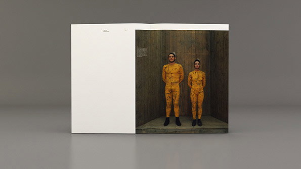 An open book shows a photograph of two people standing side by side in a concrete room. They wear matching yellow, textured jumpsuits and dark boots.