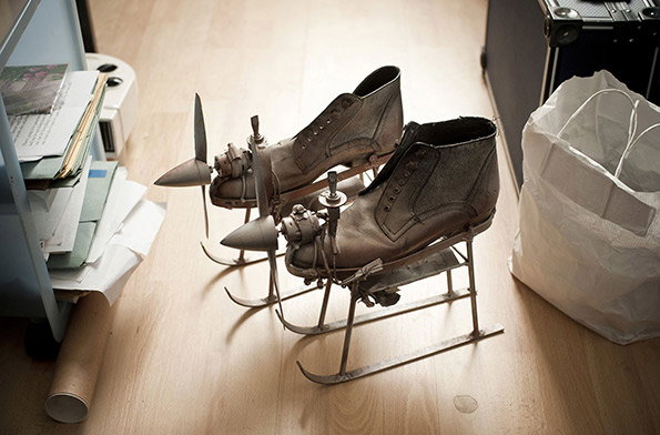 A pair of brown leather boots modified into flying machines. Each boot is mounted on metal skids and fitted with a small engine and propeller.
