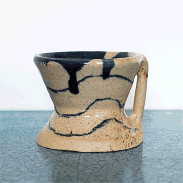 A ceramic cup with a thick handle and a flared base. The cream-coloured glaze is decorated with abstract, dripping streaks of dark blue.