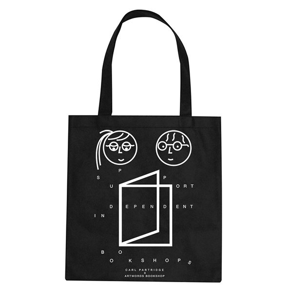 A black tote bag featuring a white graphic of two faces and an open book. Text arranged around the illustration reads “Passport Independent in Bookshops” and “Carl Partridge Artwords Bookshop”.