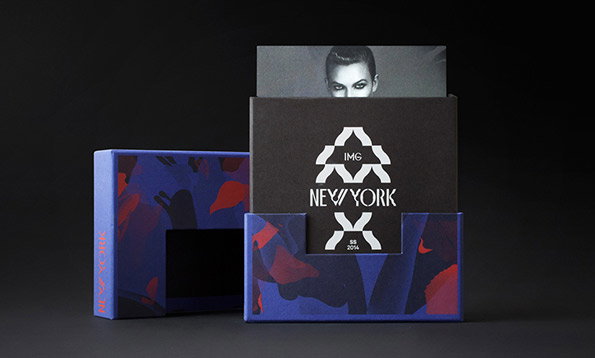 A blue patterned box holds a black card with a white logo and the words “IMG NEW YORK”. A black and white portrait of a person peeks out from behind the card.