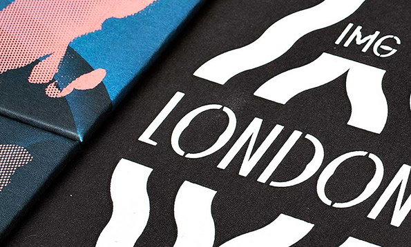 A close-up of two printed materials. One is a black surface with white stencil-style text that reads “LONDON” and “IMG”. The other is a blue and pink graphic with a halftone dot pattern.