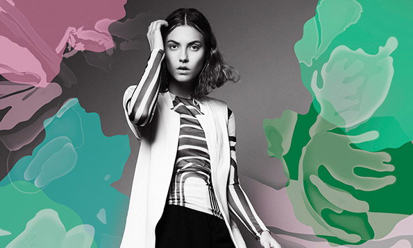 A person in a striped top and white coat poses with one hand to their head. They are framed by abstract, fluid shapes in shades of pink and green.