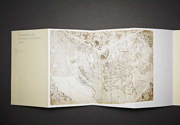 An open accordion-fold book displays an aged, sepia-toned map of the world. Text on the left page reads “Planisphere by Giovanni Contarini, 1506”.