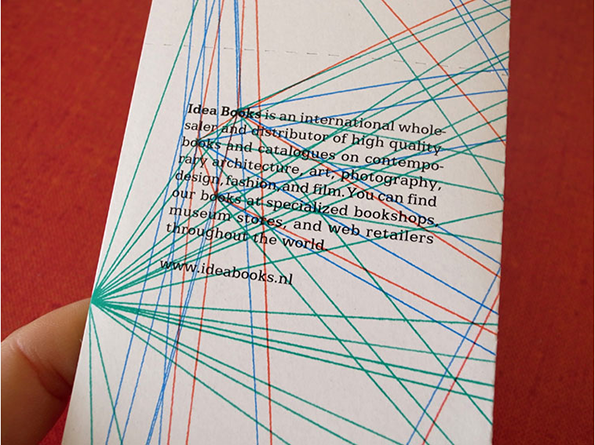 A white card features a network of thin, intersecting lines in blue, red and green. Text in the centre reads “Idea Books is an international wholesaler and distributor of high quality books and catalogues” and includes the website “www.ideabooks.nl”.