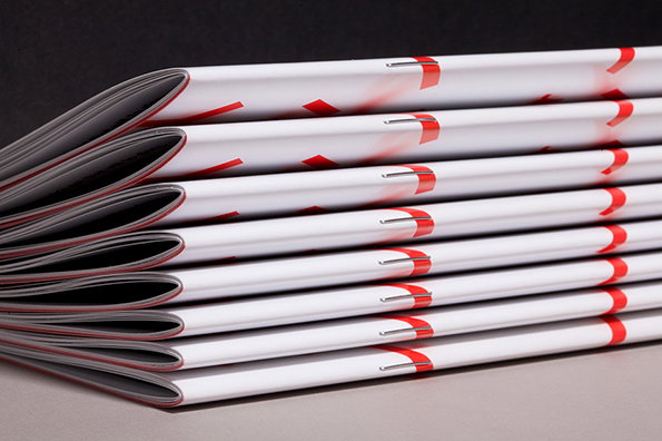 A stack of white booklets with red graphic elements on the covers. The booklets are neatly piled, showing their folded spines and stapled edges.