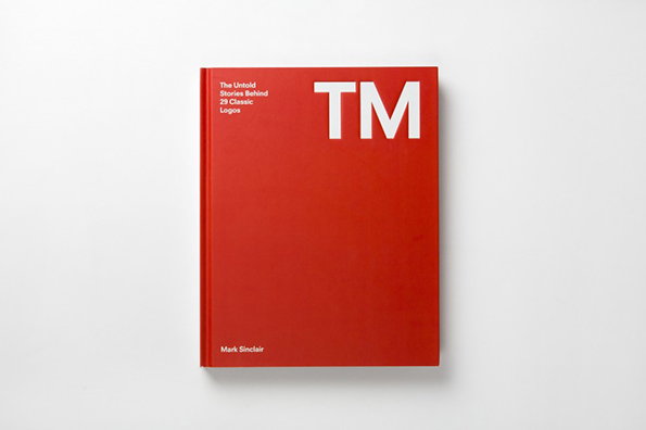 A bright red book cover features the large white letters “TM” in the top right. Text in the top left reads “The Untold Stories Behind 29 Classic Logos”, with the author “Mark Sinclair” at the bottom.