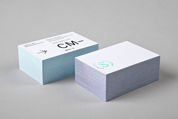 Two stacks of business cards sit on a plain grey surface. The left stack features a logo reading “CM–” and the text “Critical Mass Studio”.