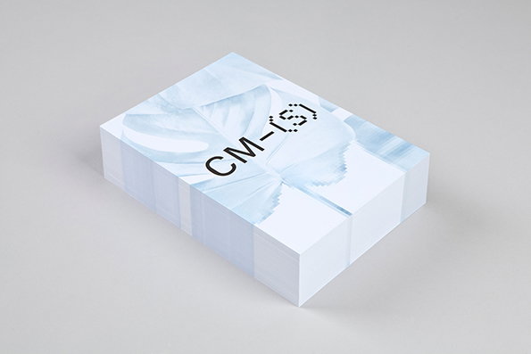 A thick stack of white cards rests on a grey surface. The top card features a pale blue image of a leaf and the text “CM-(S)”.
