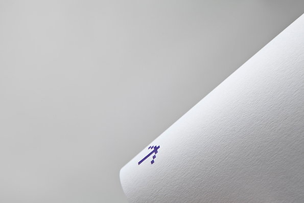 A close-up of a thick, white textured paper roll. A small, purple pixelated logo is printed on the curved edge.