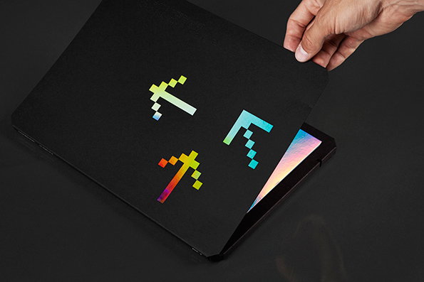 A person’s hand lifts the cover of a black folder to reveal a colourful page inside. The cover features three pixelated arrow shapes in a rainbow gradient.