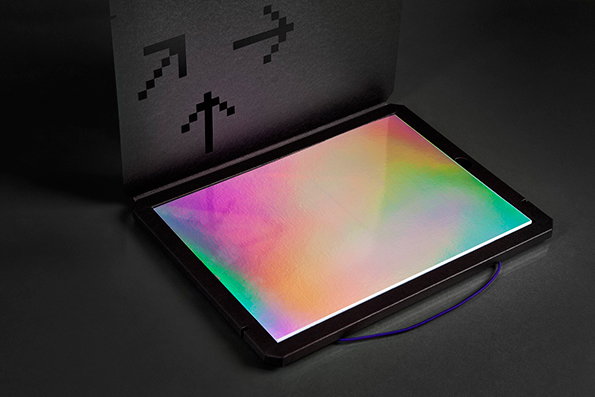A tablet lies flat on a dark surface, its screen glowing with a soft, iridescent gradient of pink, yellow and green. Behind it, a black folder stands upright, featuring three pixelated arrows pointing upwards.
