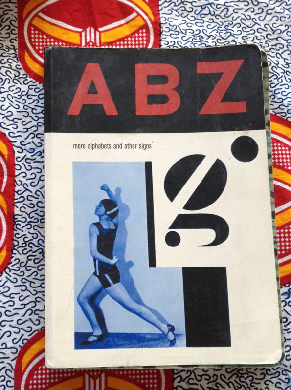 The cover of a book titled “ABZ” in bold red letters against a black background. Below, a person in a dark swimsuit poses in a blue-tinted photograph next to a large, abstract black glyph.