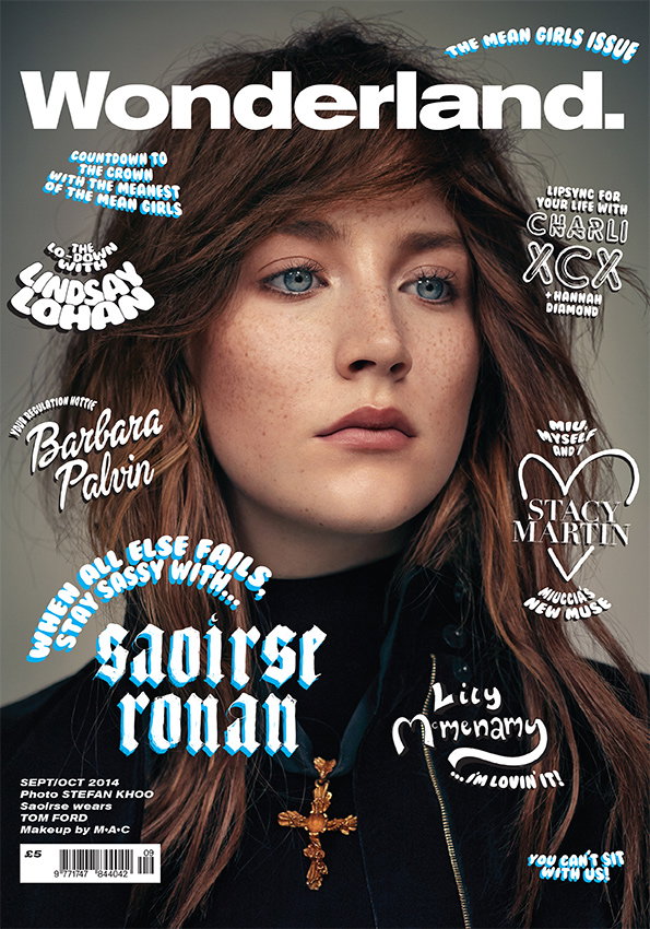 The cover of Wonderland magazine featuring a close-up portrait of Saoirse Ronan. She looks directly at the camera with a neutral expression, wearing a dark high-neck garment and a gold cross necklace. The white masthead reads “Wonderland.” and the issue is titled “The Mean Girls Issue”. Various headlines surround the subject, including “Saoirse Ronan” in bold blue lettering and “Charli XCX”.