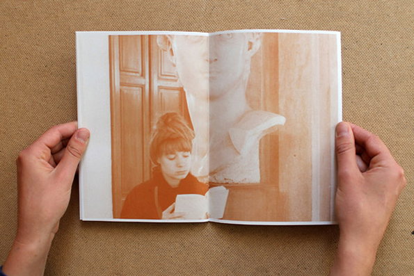 Two hands hold open a book to a double-page spread. The image shows a person reading a small book, overlaid with a large, pale bust of a classical figure.