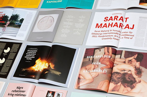 An overhead shot of several open magazines and brochures laid out on a grey surface. One spread features a large red headline reading “ Sarat Maharaj”, while another shows a photograph of a bonfire against a black background.