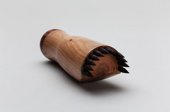 A carved wooden object with a smooth, rounded body. One end is fitted with a row of sharp, dark wooden spikes.