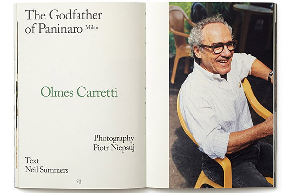 An open magazine spread featuring a portrait of Olmes Carretti. He is smiling and wearing glasses and a white shirt, seated in a yellow chair. The opposite page reads “The Godfather of Paninaro Milan” and “Olmes Carretti”, with credits for photography by Piotr Niepsuj and text by Neil Summers.