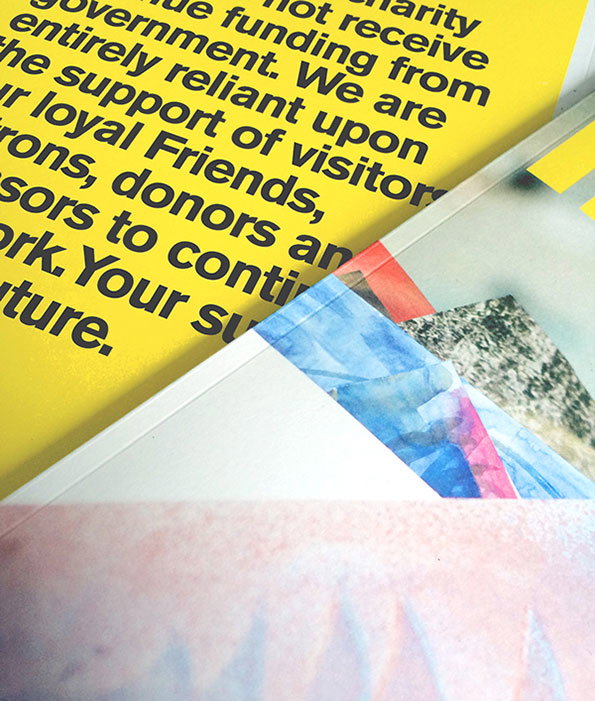 A close-up of a printed publication. One page is bright yellow with black text that reads, “We are entirely reliant upon the support of visitors”. The opposite page features a colourful, abstract collage.
