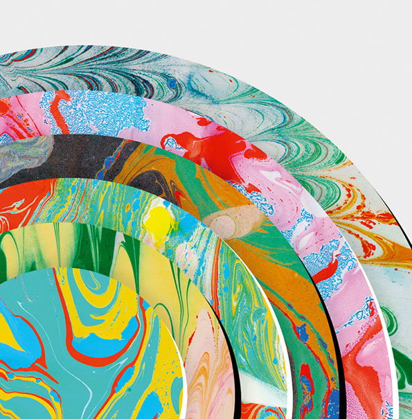 A series of circular marbled papers are layered and fanned out against a plain white background. Each sheet features swirling, organic patterns in a different vibrant colour palette.