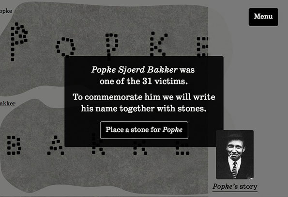 A screenshot of a digital memorial. A black pop-up box reads “Popke Sjoerd Bakker was one of the 31 victims. To commemorate him we will write his name together with stones.” Below the text is a button that says “Place a stone for Popke”. In the background, the name “Popke Bakker” is spelled out in small stones, alongside a small black-and-white portrait of a person.