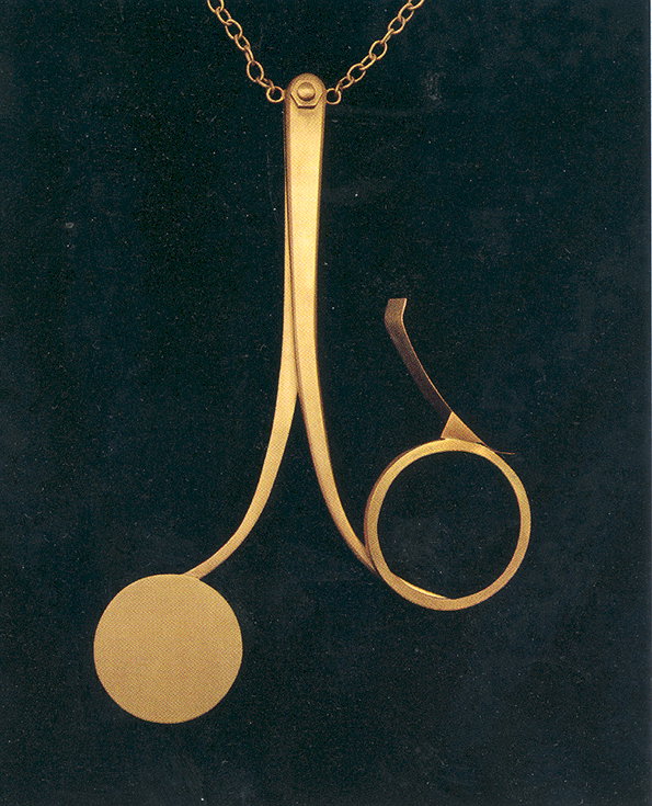 A gold pendant hangs from a delicate chain against a dark background. The piece features two sweeping curves that end in a solid circle and an open ring.