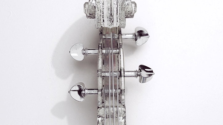 A close-up of the headstock of a transparent violin made from glass or acrylic. The clear material catches the light, showing the strings and silver tuning pegs against a plain white background.