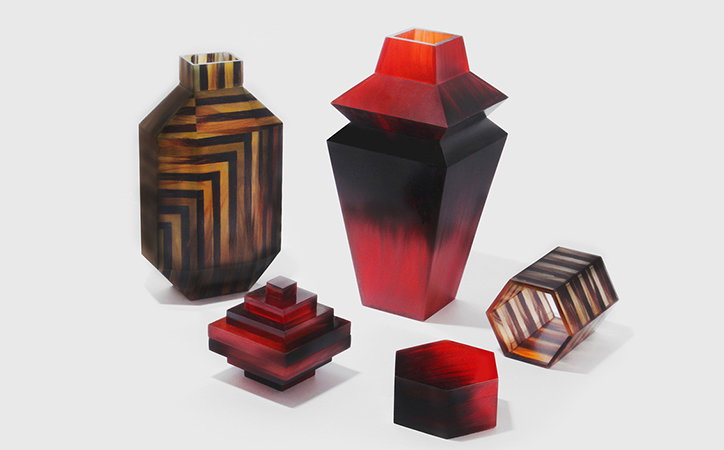 A collection of geometric vases in red and brown tones against a plain white background. Some feature bold linear stripes, while others have a smooth, gradient finish.