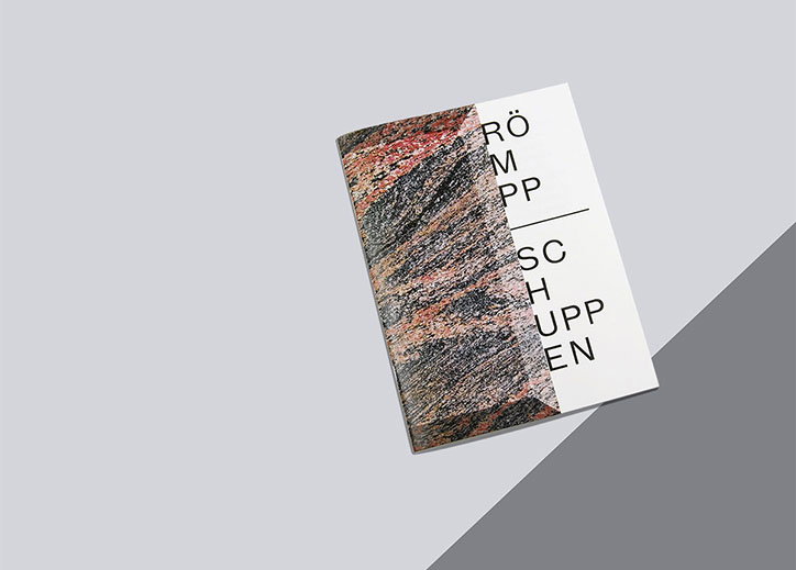 A booklet lies on a grey surface, its cover split between a textured, marbled image and a white section. Black typographic text on the white side reads “RÖMPP” above a thin line and “SCHUPPEN” below.